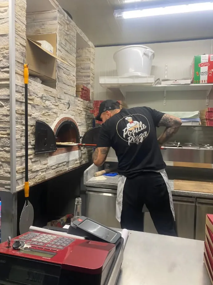 Pizzaïolo Popille Pizza enfournant une pizza dans le four à bois